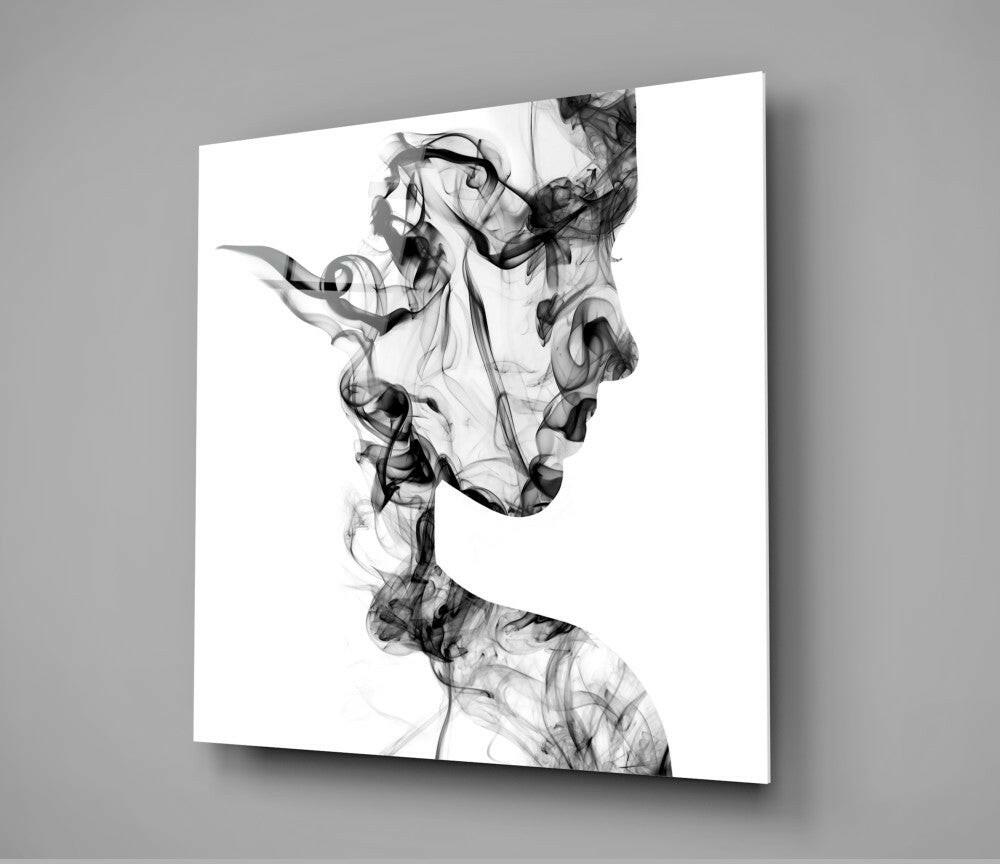Black smoke wisps form two overlapping profile silhouettes on white glass mounted on gray wall.