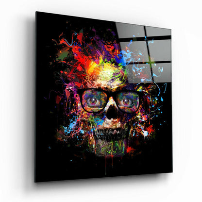 Colorful skull with glasses displayed on black glass panel, viewed at an angle showing vibrant paint splatter effects in reds, blues, yellows, and purples against dark background.