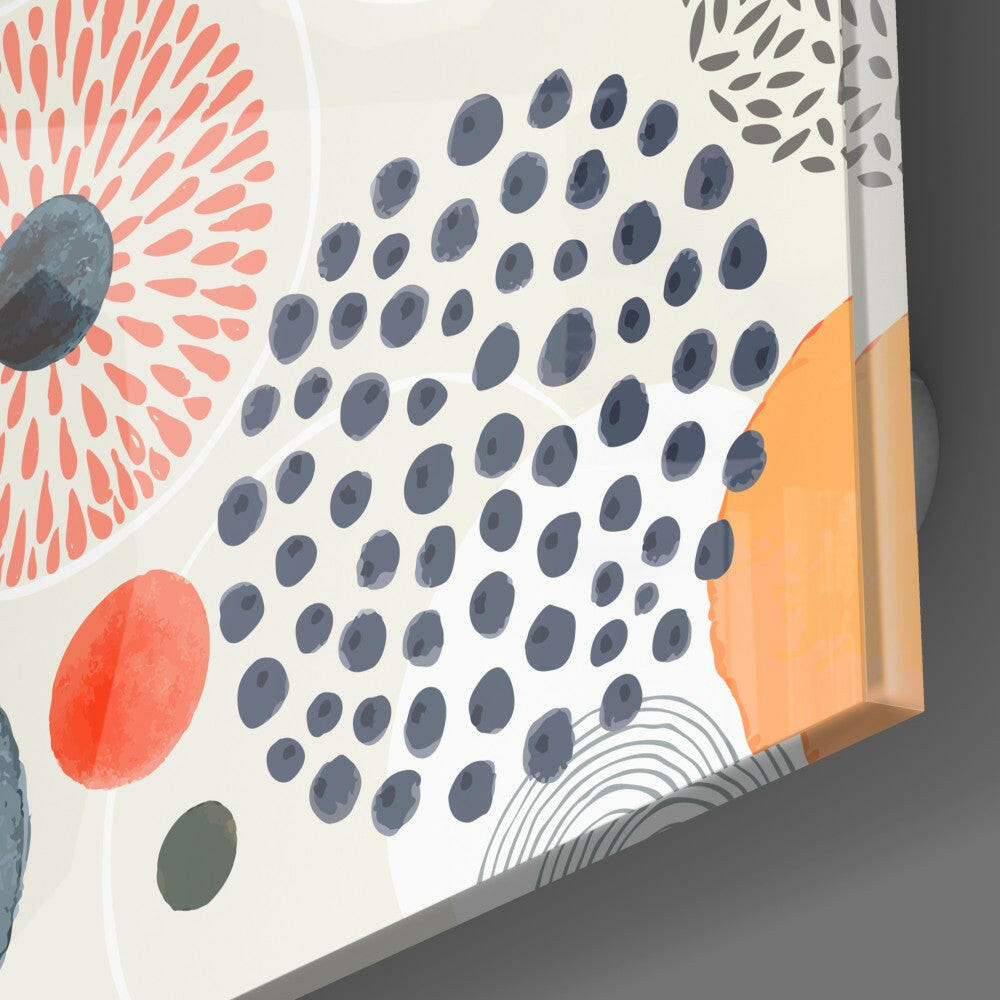Close-up angled view of glass wall art showing central blue dot pattern surrounded by coral radiating lines, red oval, orange rectangle, and gray leaf designs on white background.