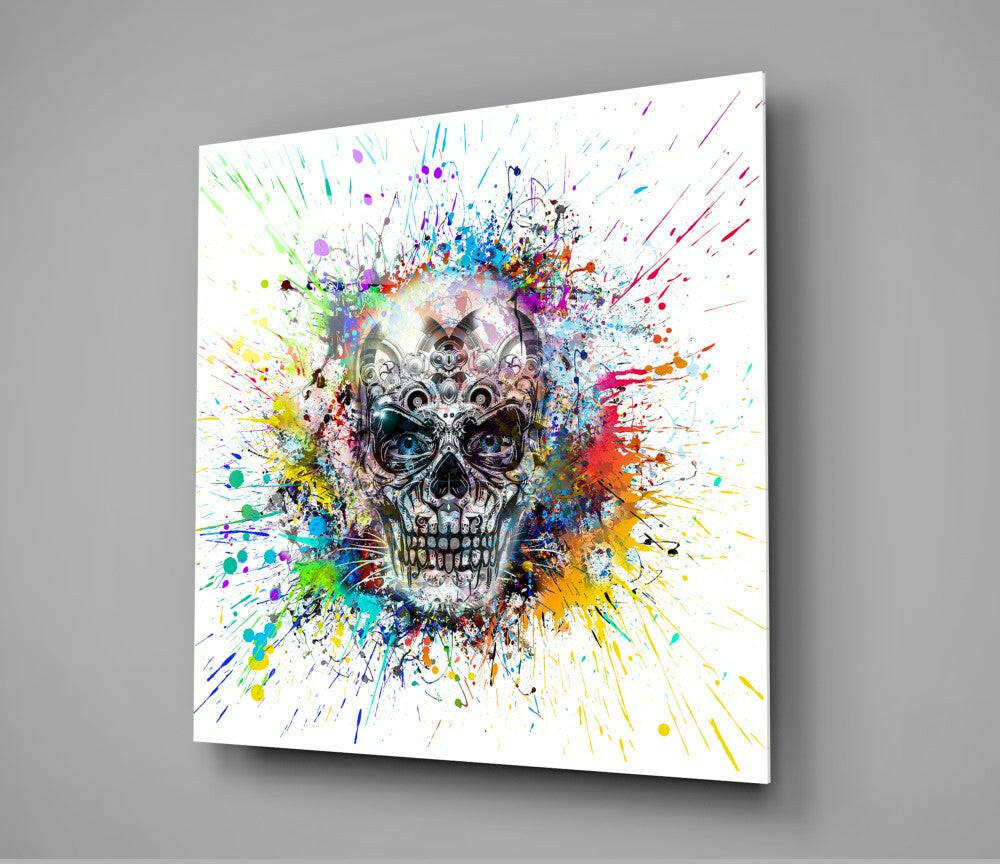 Angled view of glass wall art featuring a detailed mechanical skull centered on white background with vibrant multicolored paint splatters radiating outward.
