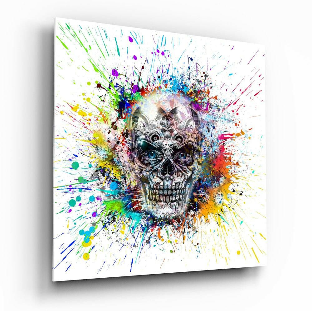 Angled perspective of glass wall art displaying an ornate mechanical skull surrounded by radiating multicolored paint splatters on white background.