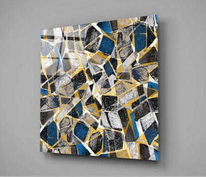 Square glass wall art with geometric honeycomb pattern in blue, gold, black, white, and gray segments displayed at an angle.
