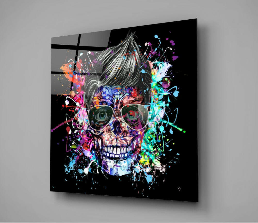 Colorful skull with sunglasses and spiked hair on black glass panel, displayed at angle against gray wall.