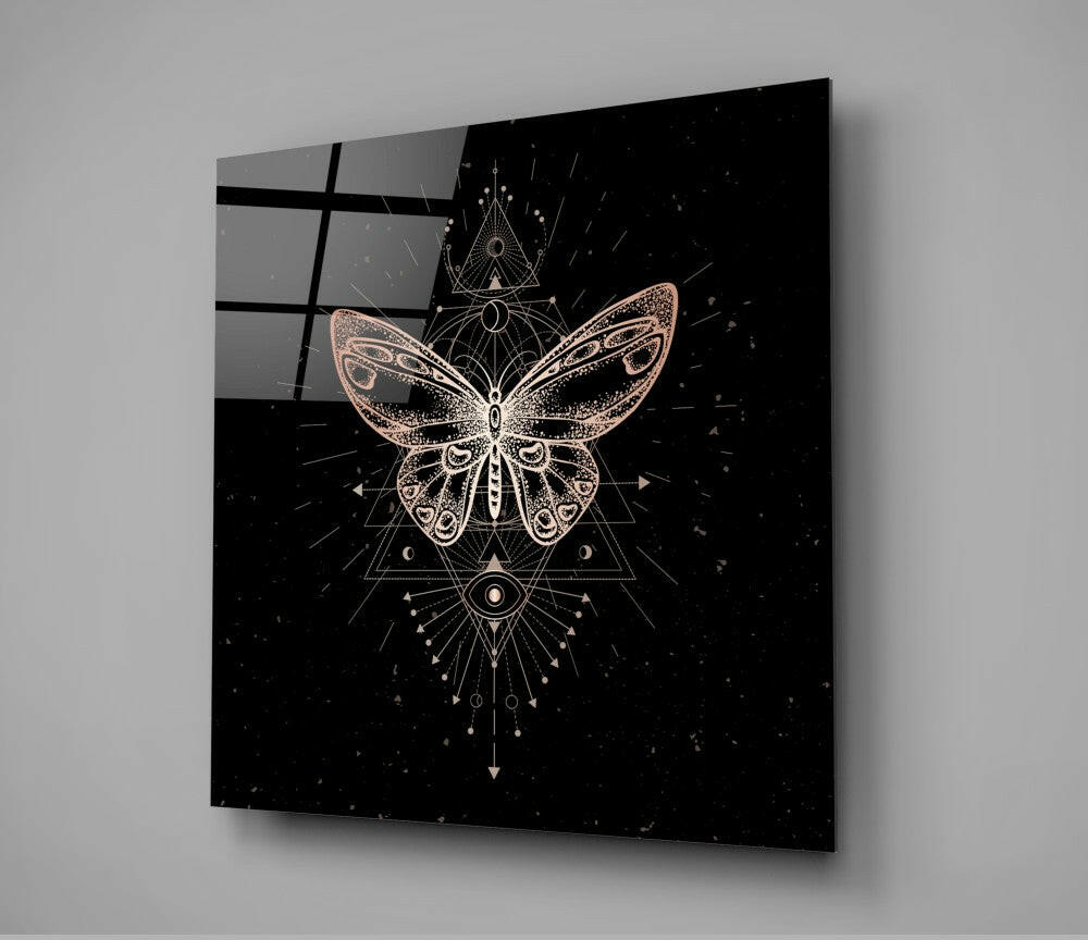 Angled view of square glass wall art displaying a copper and white butterfly with geometric sacred geometry symbols on black background.