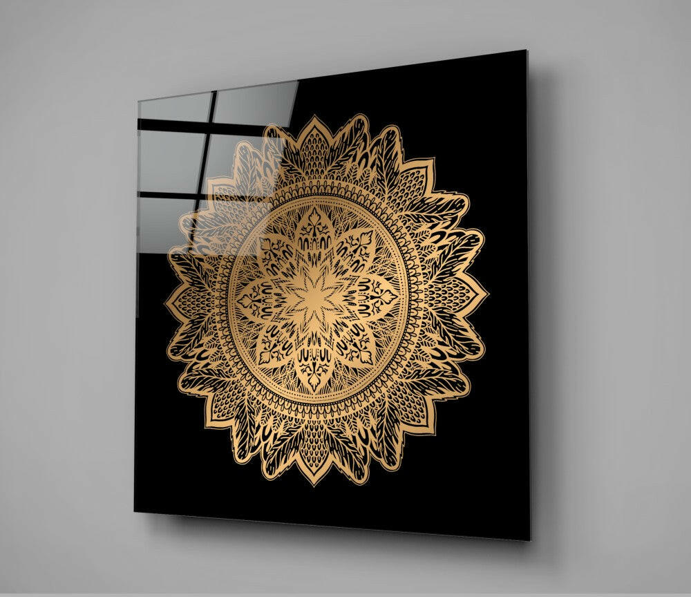Gold ornate mandala design on black glass panel mounted on white wall, angled perspective view.