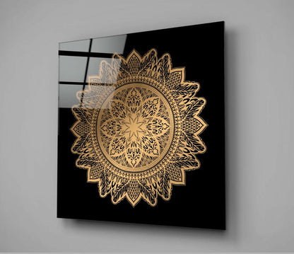Gold ornate mandala design on black glass panel mounted on white wall, angled perspective view.