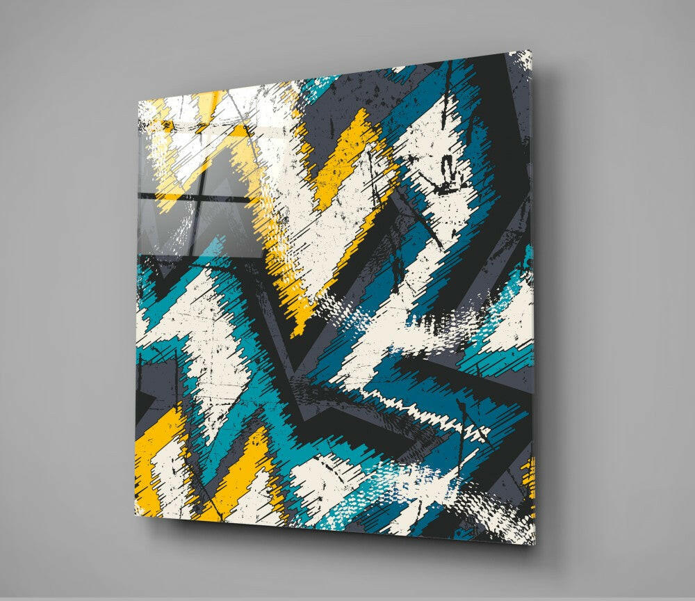 Abstract geometric glass wall art with diagonal brushstroke pattern in teal, yellow, white, and charcoal, mounted on gray wall.