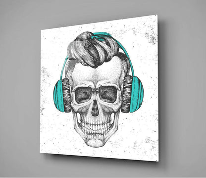 Angled front view of glass wall art featuring a monochrome skull illustration wearing turquoise headphones and dark sunglasses on a white speckled background.