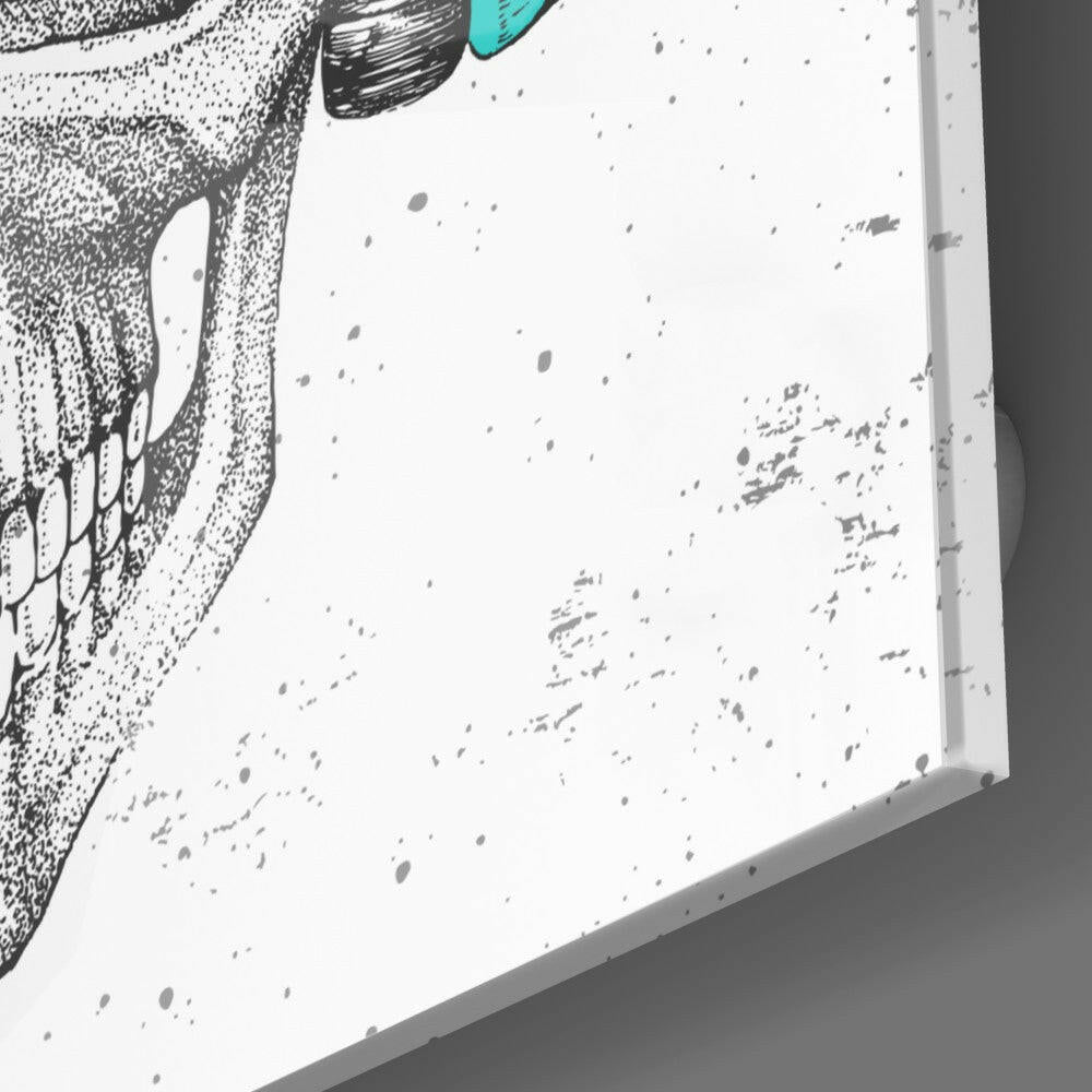 Close-up angled view of white glass wall art with black stippled skull design and turquoise accent detail.