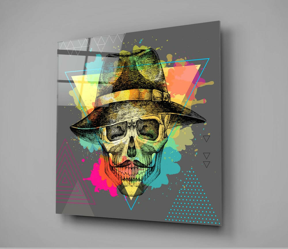 Glass wall art panel displaying a skull wearing a wide-brimmed hat, surrounded by colorful watercolor splashes and geometric shapes on dark gray background.