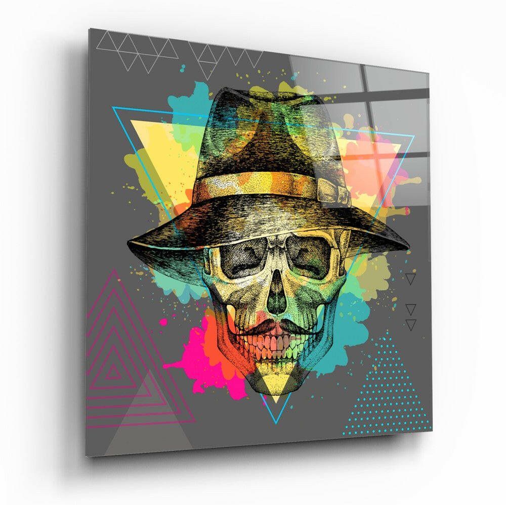 Angled view of glass wall art displaying a colorful skull wearing a fedora hat against a gray background with geometric shapes and vibrant splashes of cyan, yellow, magenta, and green.