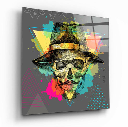Angled view of glass wall art displaying a colorful skull wearing a fedora hat against a gray background with geometric shapes and vibrant splashes of cyan, yellow, magenta, and green.