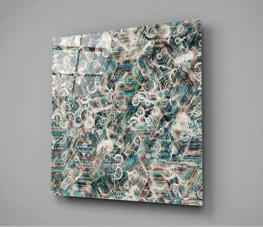 Square glass wall art panel mounted at an angle displaying an abstract pattern of circular shapes and layered textures in teal, cream, and rust tones.