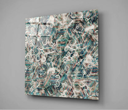Square glass wall art panel mounted at an angle displaying an abstract pattern of circular shapes and layered textures in teal, cream, and rust tones.