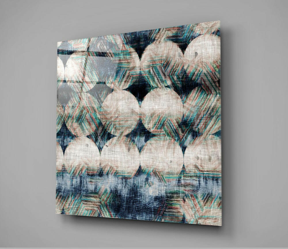 Square glass wall art panel displaying overlapping cream and teal patterned fabric design with dark blue accents, mounted at angle against gray background.