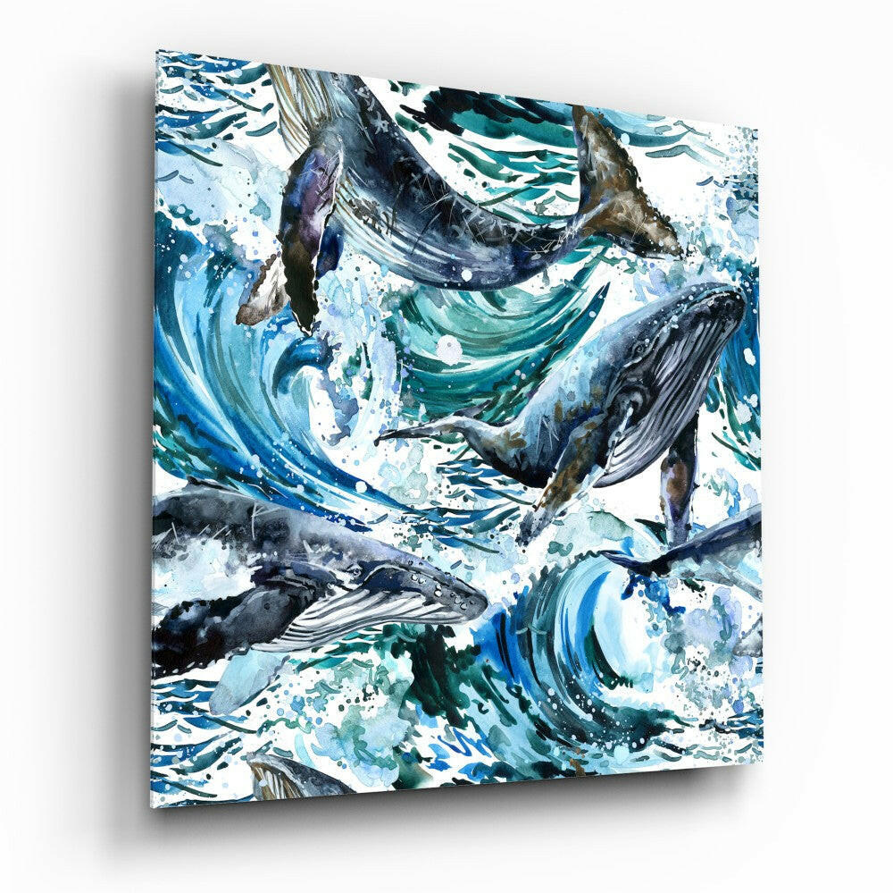 Glass wall art featuring multiple whales in dynamic blue and teal watercolor swirls with splashing white accents, angled to show depth and shadow.