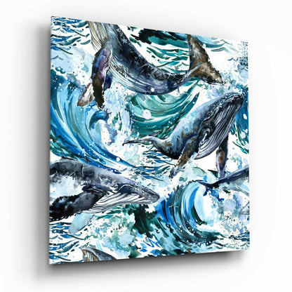 Glass wall art featuring multiple whales in dynamic blue and teal watercolor swirls with splashing white accents, angled to show depth and shadow.