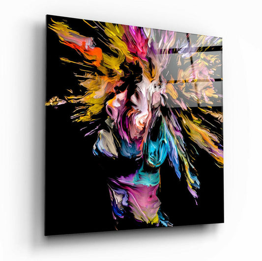 Angled view of a glass wall art panel featuring an abstract colorful portrait with yellow, pink, purple, and blue paint-like brushstrokes against black background.