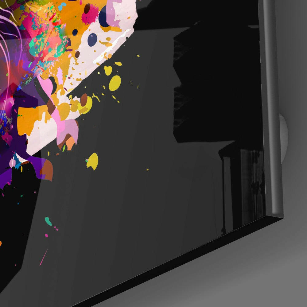 Colorful abstract lion head glass wall art mounted on dark wall, viewed at an angle showing vibrant paint splatters in purple, yellow, pink, and orange.
