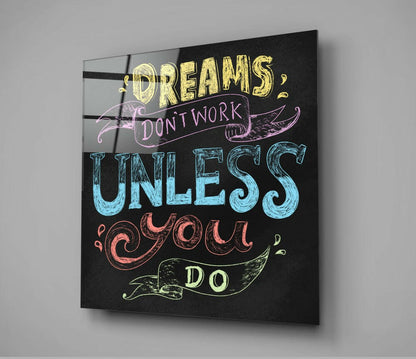 Angled view of a black canvas wall art displaying colorful hand-lettered text reading "Dreams don't work unless you do" with decorative banner elements.