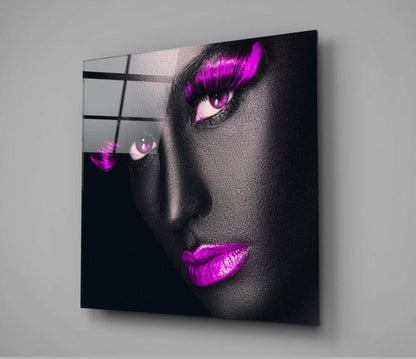 Glass wall art mounted at an angle showing a face with magenta eyeshadow, eyelashes, and lips against dark background.