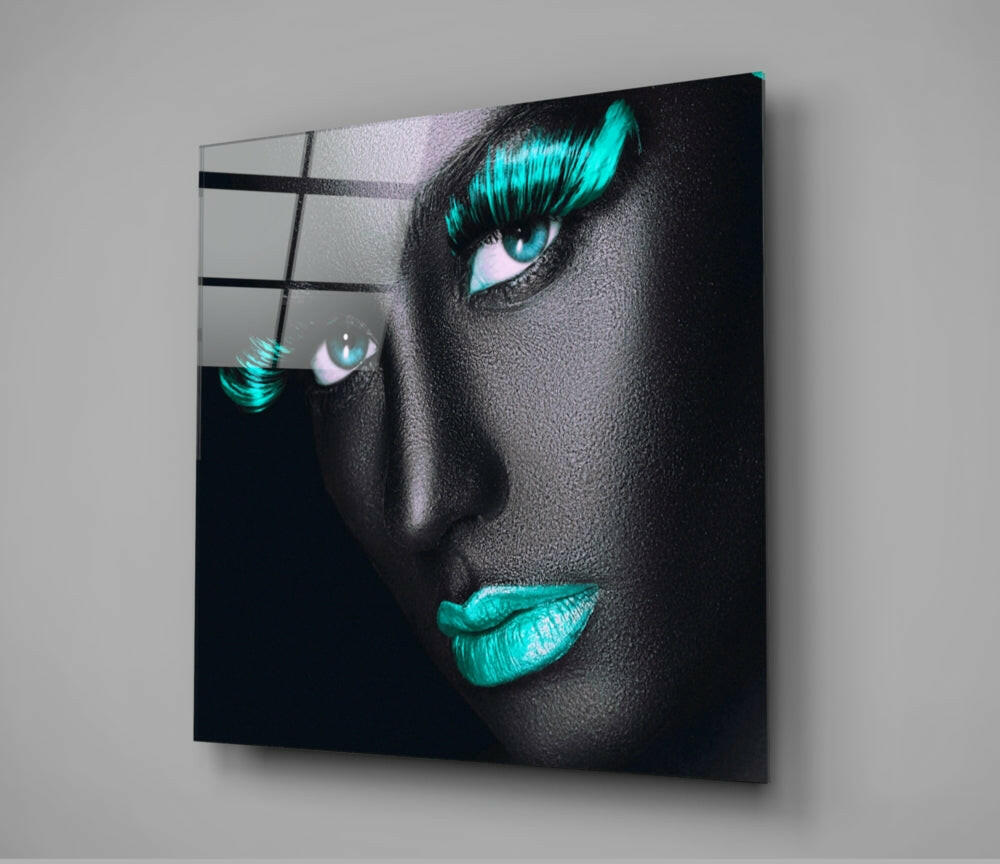 Modern glass wall art displaying a close-up portrait with turquoise eyeshadow and lips against dark skin tone.