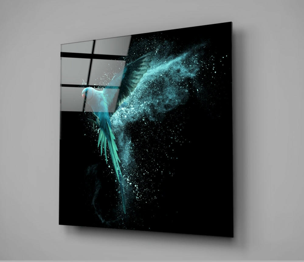 Glass wall art displaying a turquoise bird with dispersing particles against black background, mounted at angle on gray wall.