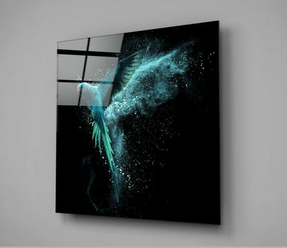 Glass wall art displaying a turquoise bird with dispersing particles against black background, mounted at angle on gray wall.