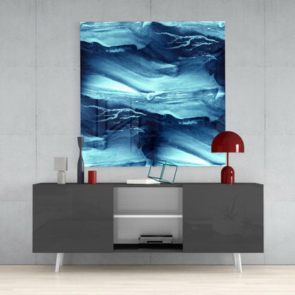 Abstract Waves Glass Wall Art in shades of blue and white displayed above a gray media console with red lamp and accessories.