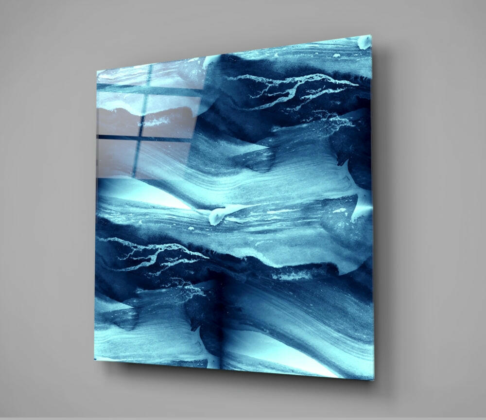 Square glass wall panel displaying layered abstract waves in shades of blue, teal, and white with visible brushstroke texture, mounted at angle against gray background.