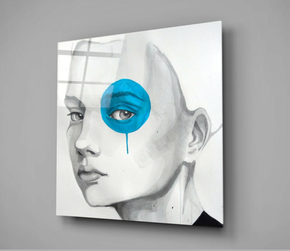 Angled view of glass wall art featuring pencil-drawn portrait with bright blue circular overlay on the eye and dripping accent.
