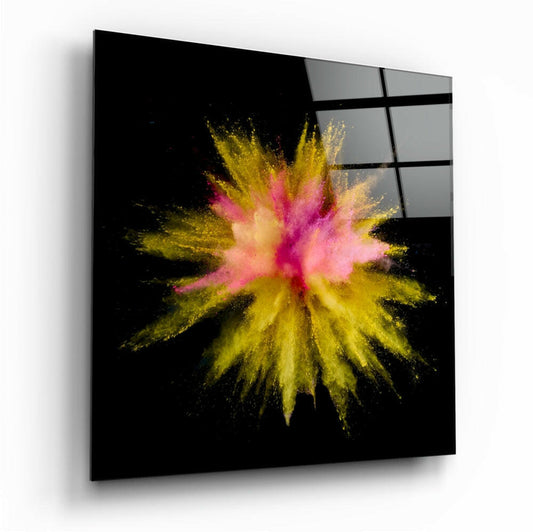 Angled view of square black glass wall art with vibrant pink and yellow powder explosion radiating from center, mounted on white wall.