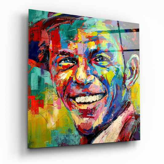 Colorful portrait of a smiling man on glass wall art with vibrant red, yellow, blue, and green paint strokes, displayed at an angle showing depth and shadow.