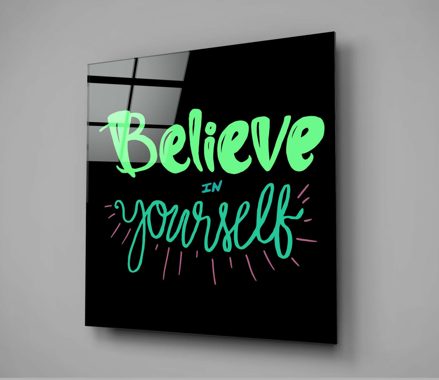 Black glass wall art with neon green and pink handwritten text reading "Believe in Yourself" displayed at an angled perspective against gray background.