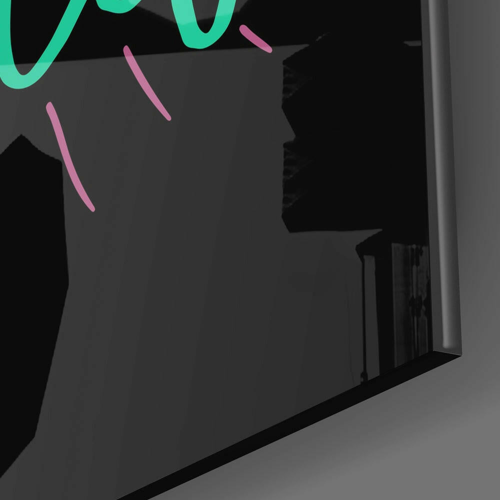 Close-up of glass wall art showing neon green and pink decorative strokes on dark gray surface with shadowed interior space visible.