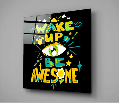 Square black glass panel displaying colorful typography art with yellow, green, and teal text reading "Wake Up & Be Awesome" surrounded by decorative illustrations, mounted on gray wall.
