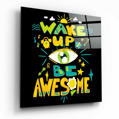 Angled view of black glass wall art with colorful yellow, teal, and green text reading "Wake Up & Be Awesome" surrounded by decorative icons including an eye, sun, and stars.