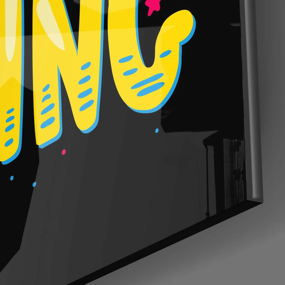 Close-up angled view of yellow glass wall art with blue outlines and dashes, displaying partial "Start Doing" text against black background.
