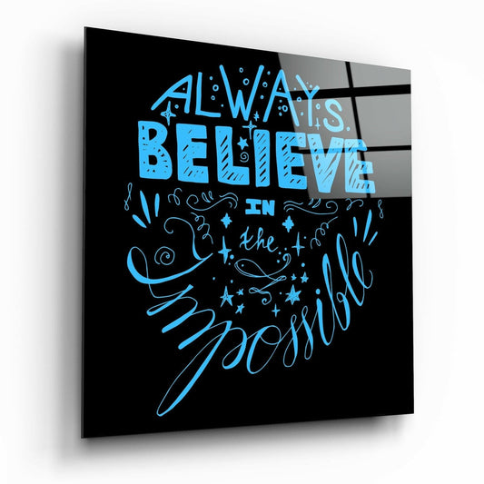 Angled perspective view of black glass wall art with bright blue neon-style lettering reading "Always Believe in the Impossible" surrounded by decorative stars and flourishes.