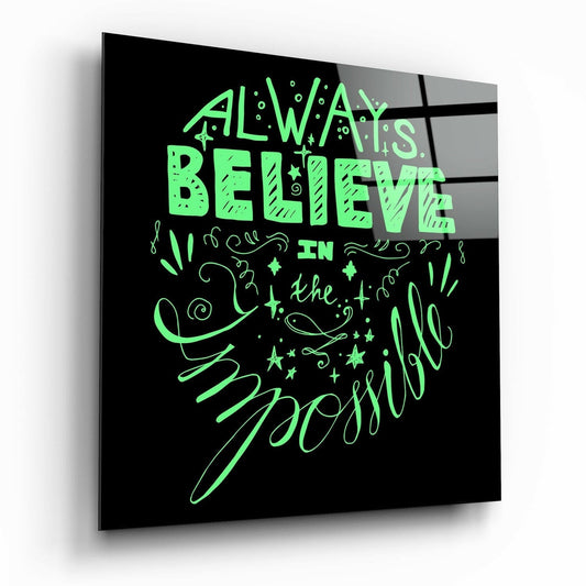 Angled perspective view of black glass wall art with bright green neon-style text reading "Always Believe in the Possible" with decorative flourishes and stars.