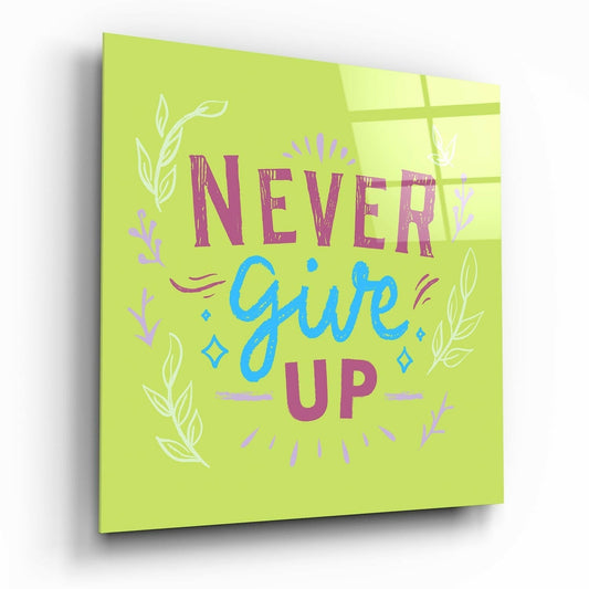 Angled view of lime green glass wall art displaying "Never Give Up" in purple and blue text with decorative leaf motifs.