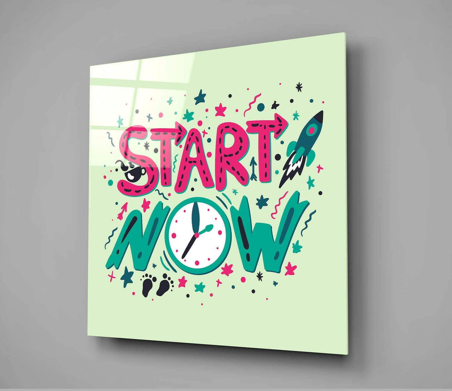 Angled view of a lime green glass wall panel with pink "START NOW" text, teal "NOW" letters, a clock face, rocket, stars, and decorative elements in pink and teal colors.