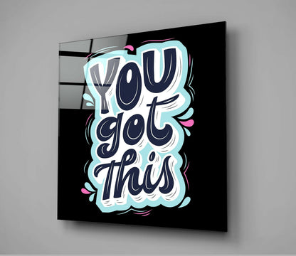 Angled view of glass wall art with navy lettering reading "You Got This" on black background, light blue cloud border and pink accents.