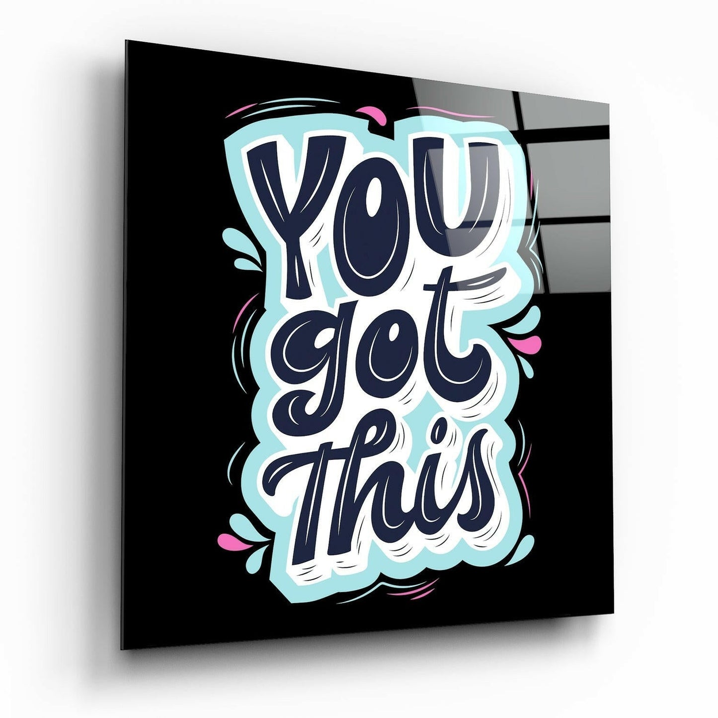 Glass wall art panel displaying "You Got This" in navy blue lettering with light blue outline and decorative pink flourishes on black background, angled three-quarter view.