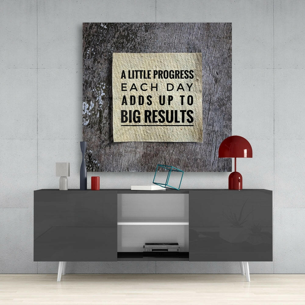 Motivational glass wall art with cream background and black text mounted above gray media console in modern interior setting.