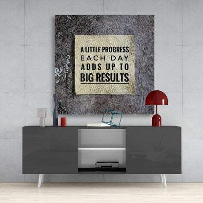 Motivational glass wall art with cream background and black text mounted above gray media console in modern interior setting.