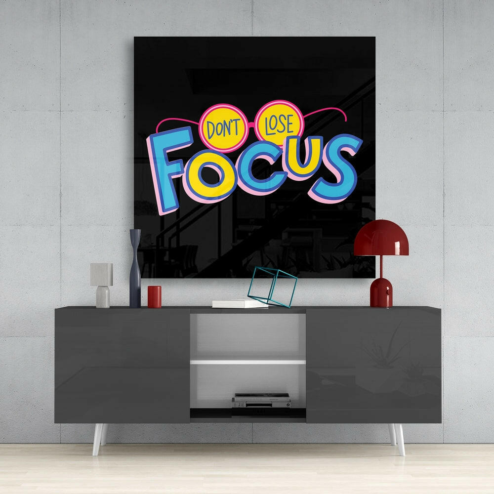Neon-style "Don't Lose Focus" glass wall art displayed above a gray media console in a modern interior setting.
