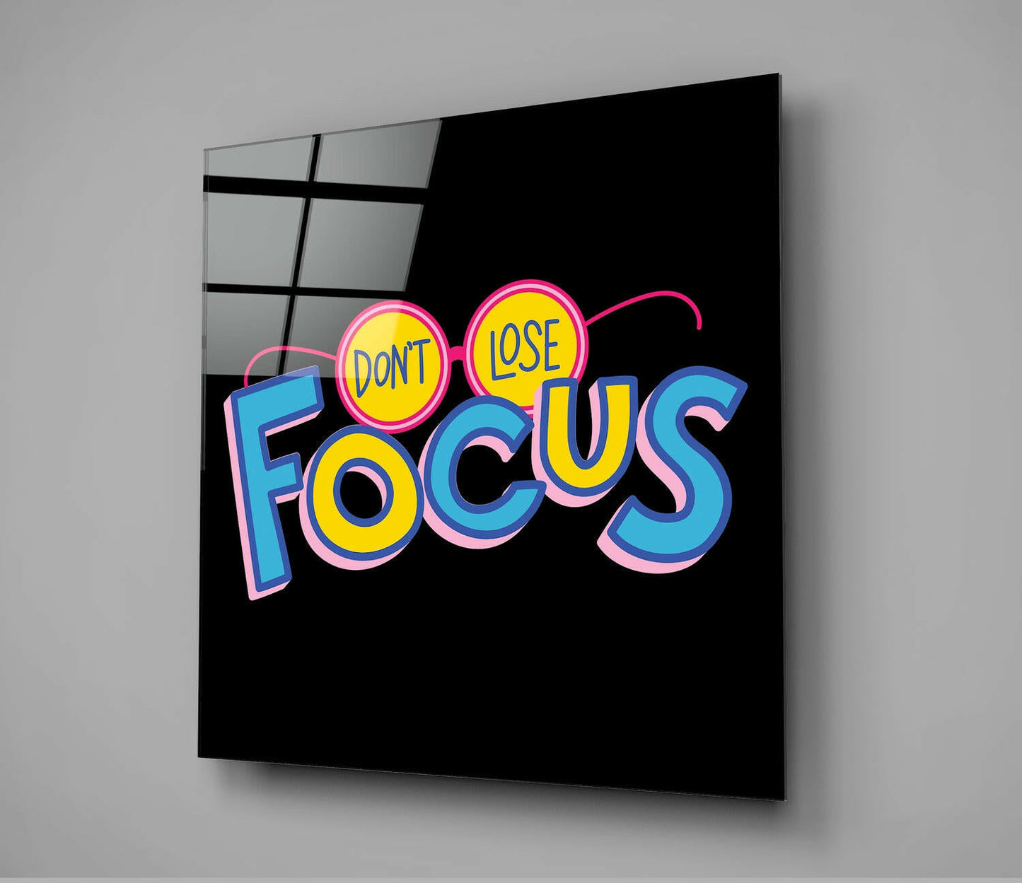 Colorful neon-style glass wall art with pink, blue, and yellow text reading "DON'T LOSE FOCUS" displayed at an angle against a gray background.