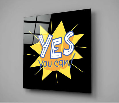 Angled front view of black glass wall art with yellow starburst design and "YES you can!" text in blue and white lettering.