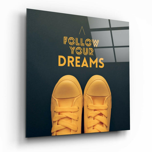 Glass wall art panel with gold text "FOLLOW YOUR DREAMS" and pair of yellow sneakers against dark teal background, angled perspective view.